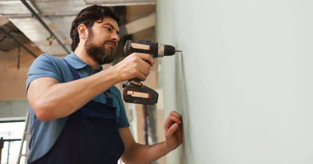 Bearded Worker Drilling Wall for Security Camera